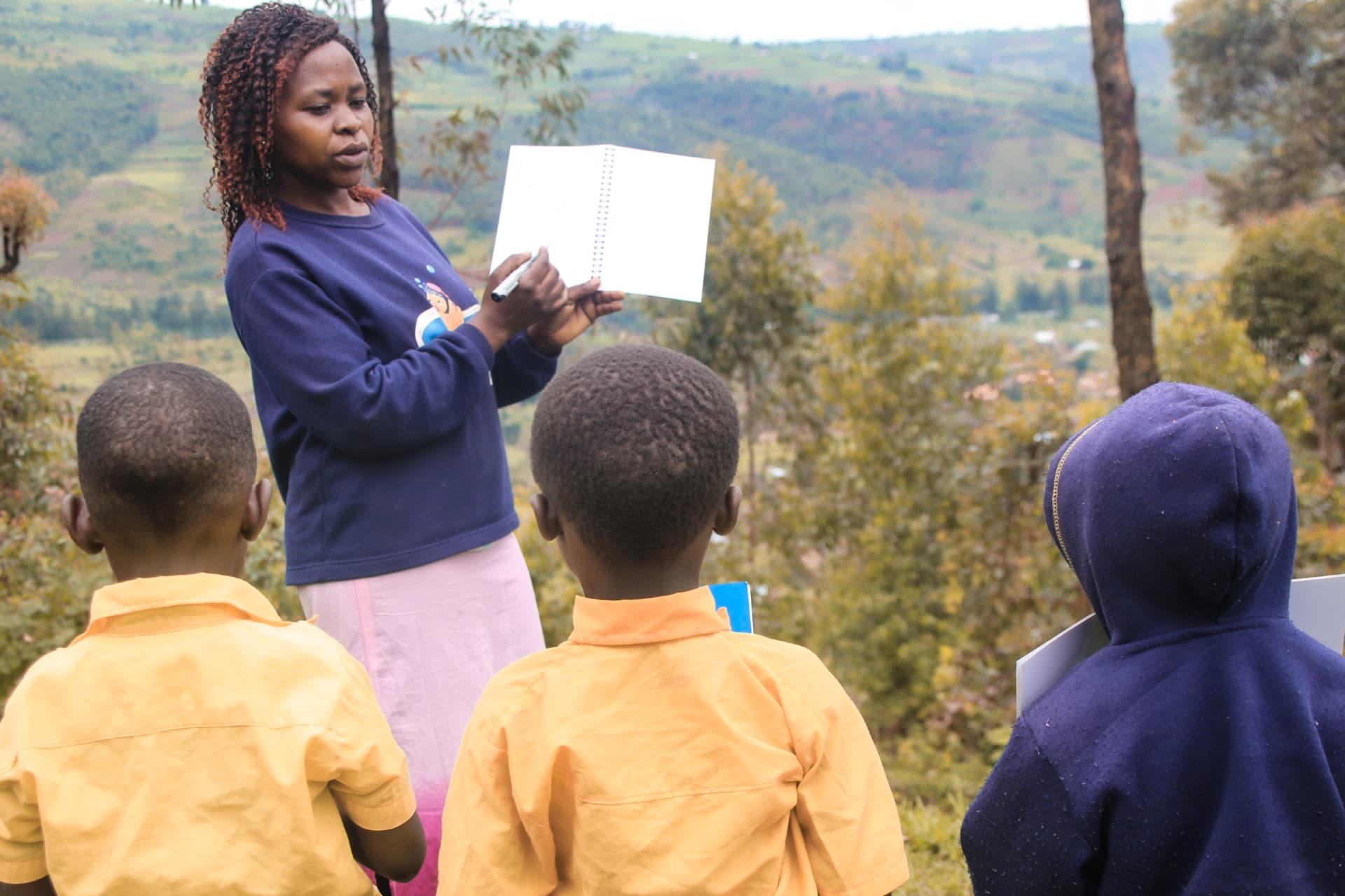 Teacher showing a Correctbook notebook to three learners on a hillside